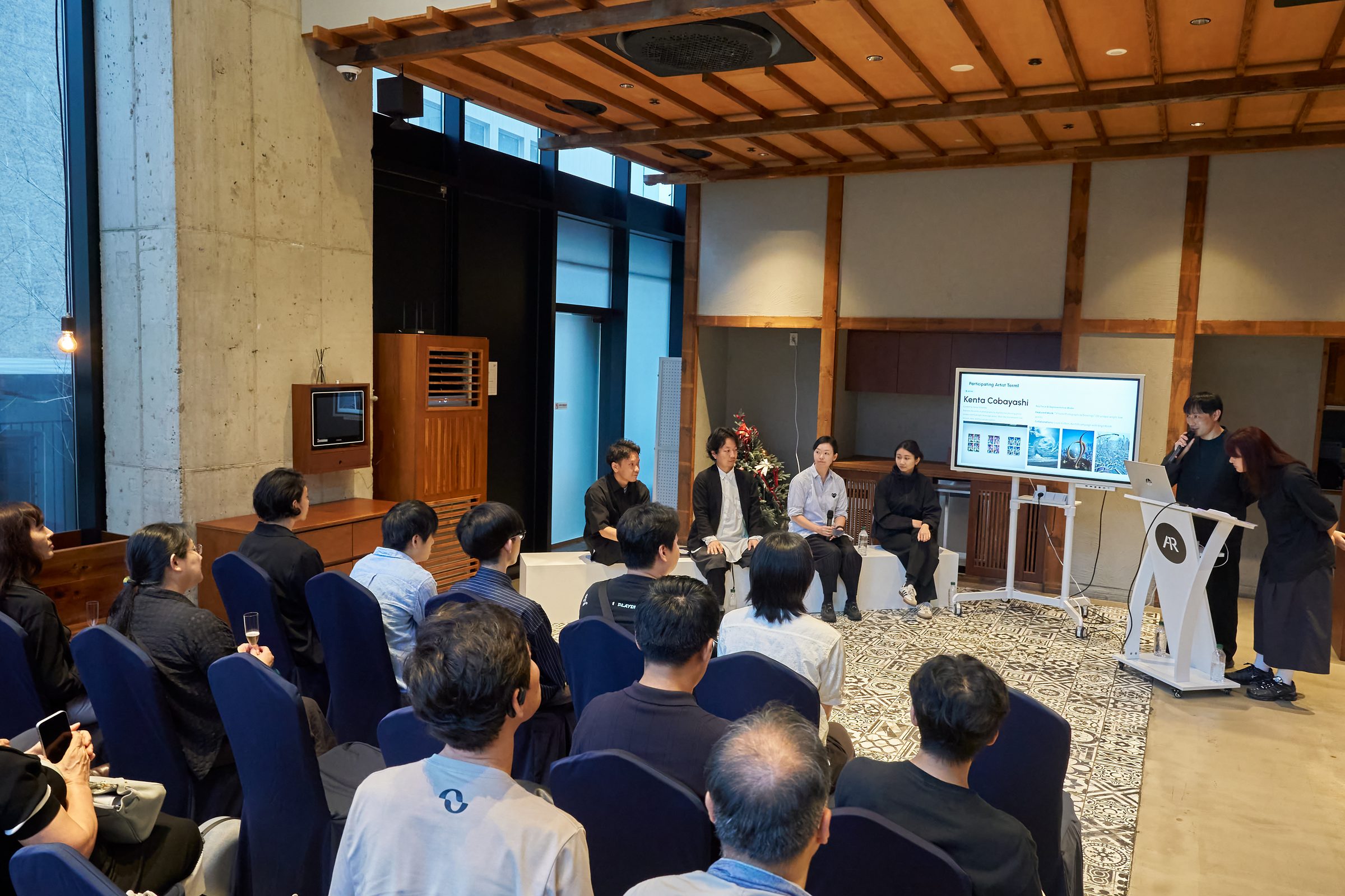 Artist talk in Seoul: artists and curators seated in front of an audience, with a presentation screen introducing the participating artists.